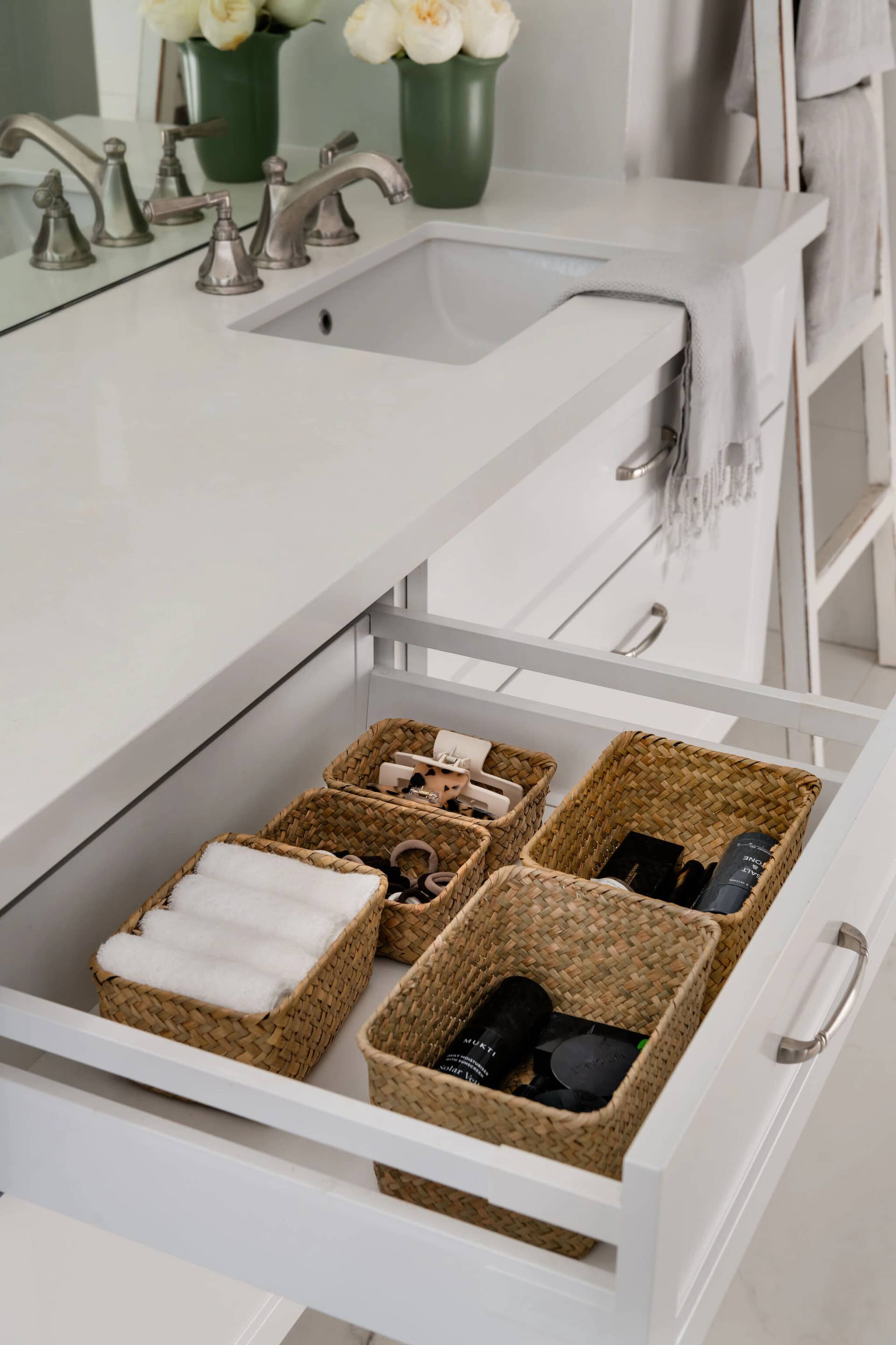 A bathroom vanity drawer with rolled towels and woven baskets