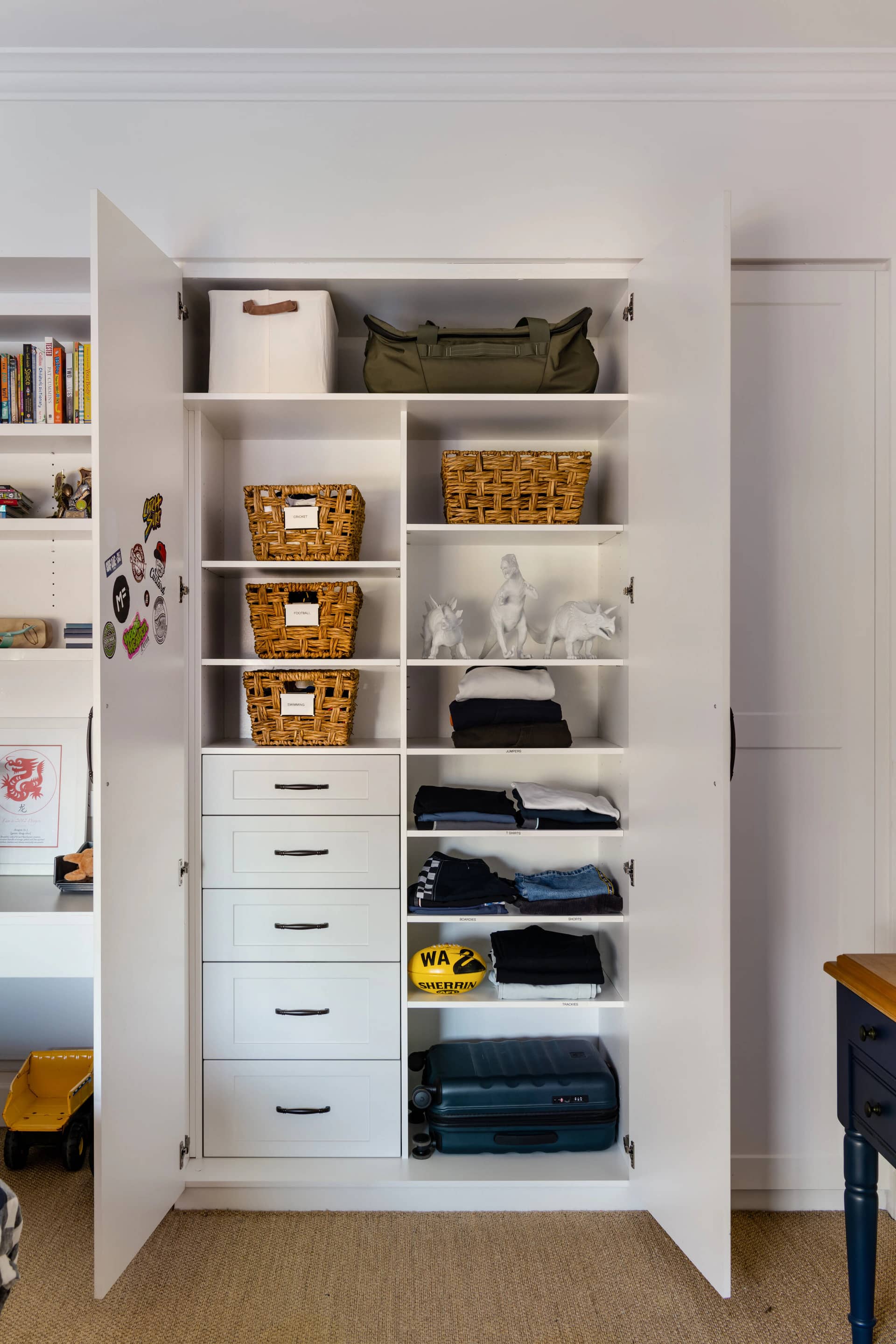 An open cupboard with folded clothes, baskets and drawers