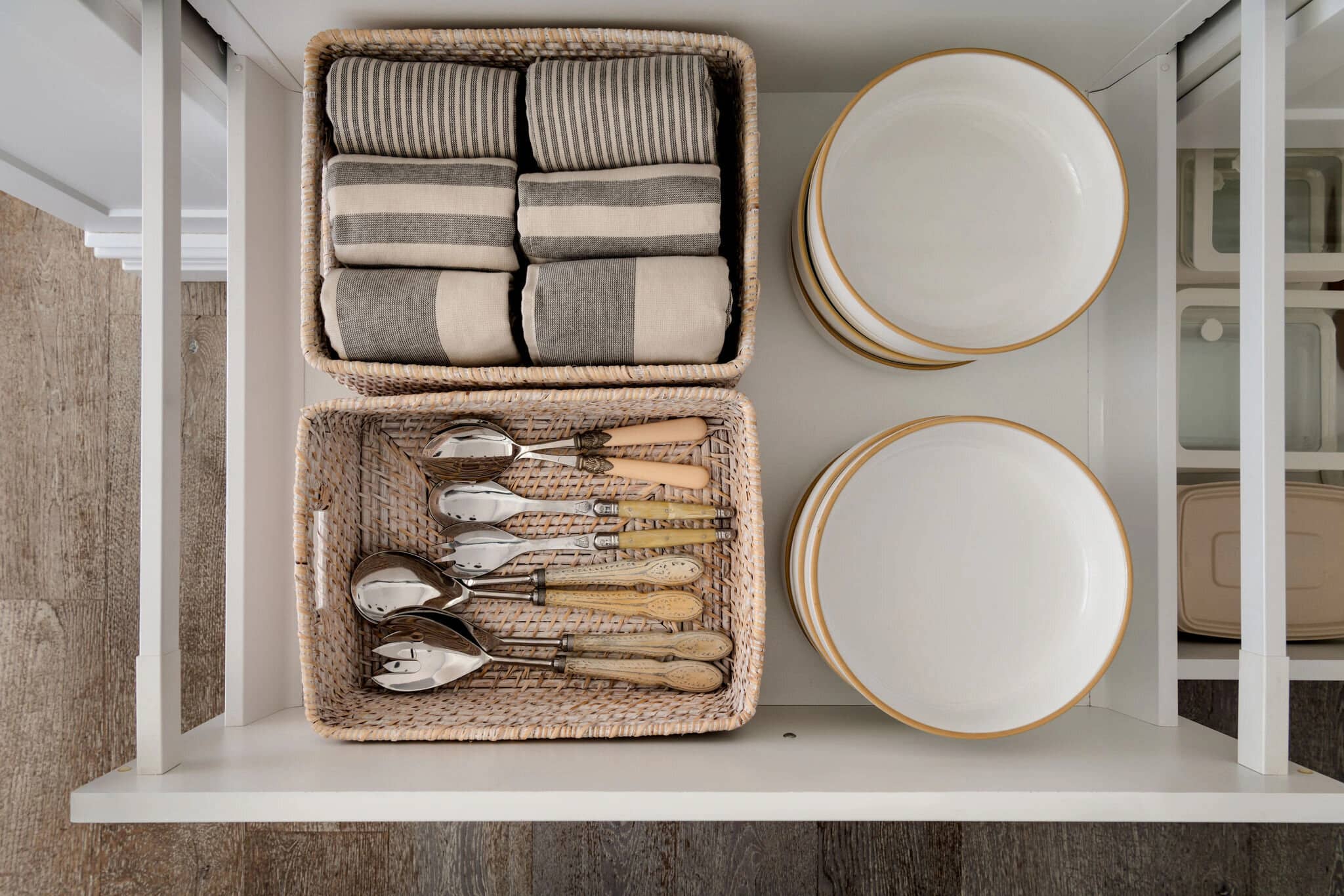 A wide kitchen drawer holding plates and cutlery in woven trays