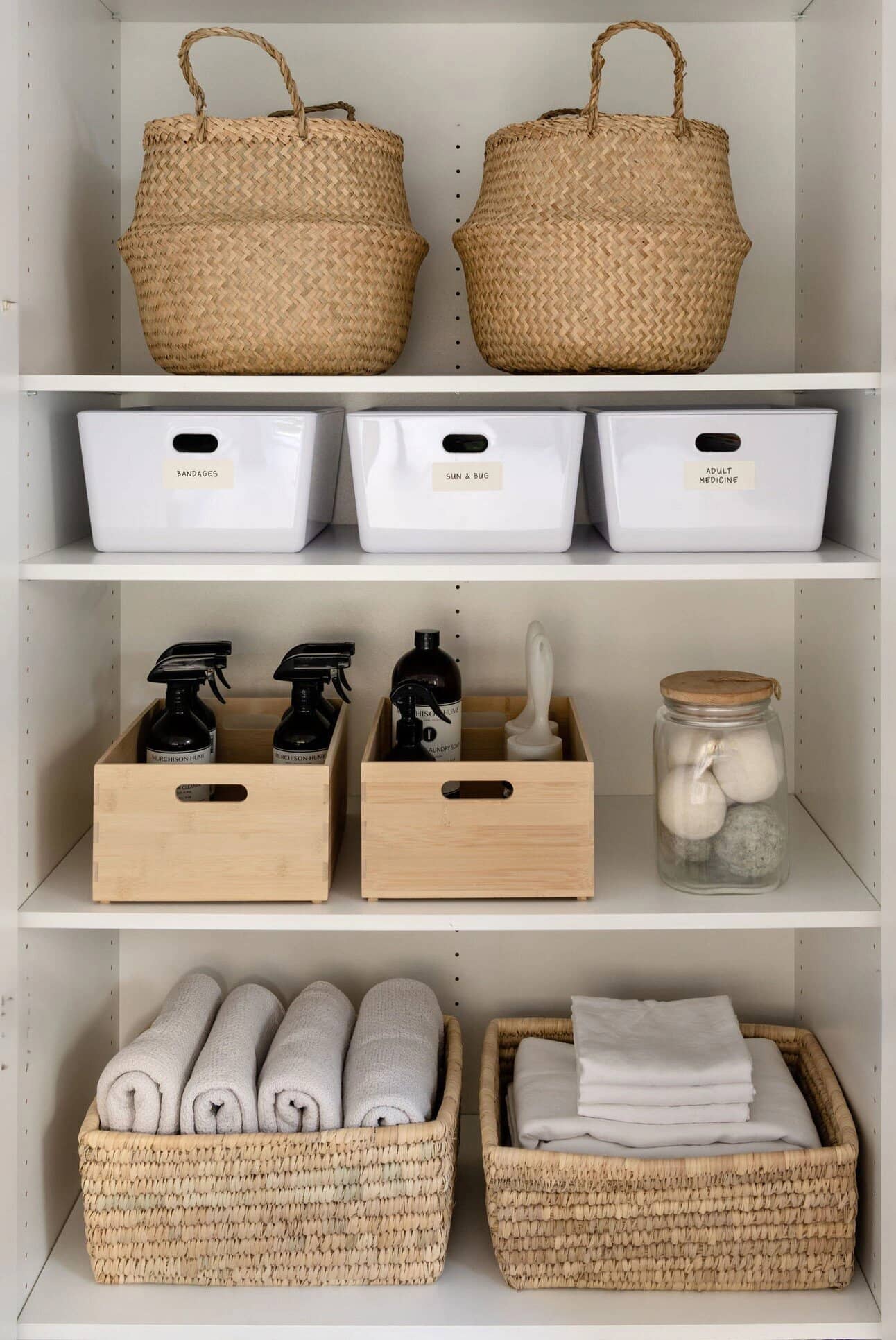 A laundry shelf with woven bags, white bins and folded linen